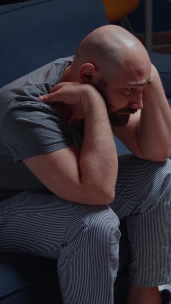 Κάθετο βίντεο: Ψυχωτικός και μόνος δυστυχισμένος, καταθλιπτικός, απογοητευμένος άντρας που κάθεται στον καναπέ νιώθοντας απογοητευμένος και ευάλωτος, που υποφέρει από αϋπνία, άγχος, ψυχικά προβλήματα, αυτοκτονικές σκέψεις - Πλάνα, βίντεο