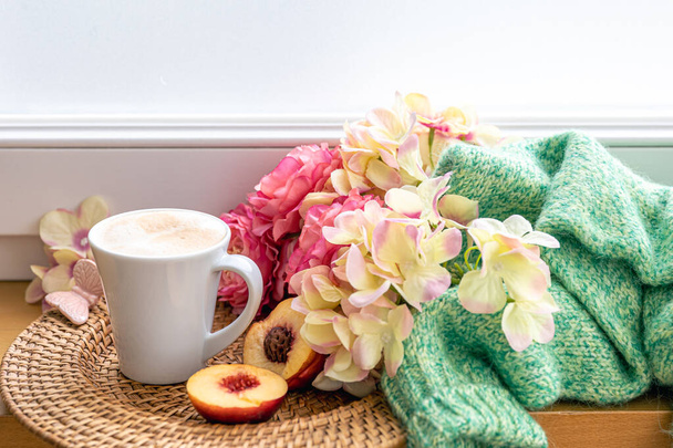 Gemütliche Eigenkomposition mit einer Tasse Cappuccino, Blumen und einem Strickelement auf verschwommenem Hintergrund. - Foto, Bild
