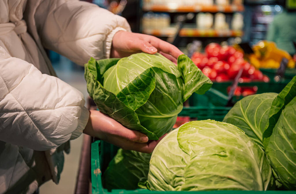 A woman chooses cabbage in a grocery store, close-up, buying organic food for cooking. - 写真・画像