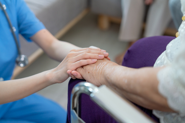 Крупним планом руки медсестри або лікаря тримають руки старшої жінки, які сидять на інвалідному візку з концепцією догляду та підтримки літніх людей в клініці або лікарняному центрі
. - Фото, зображення