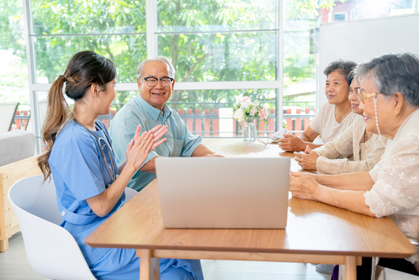 Азиатские пожилые мужчина и женщина пользуются, чтобы поговорить и весело с деятельностью медсестры или врача во время обучения с ноутбуком на столе в гостиной клиники или больницы. - Фото, изображение