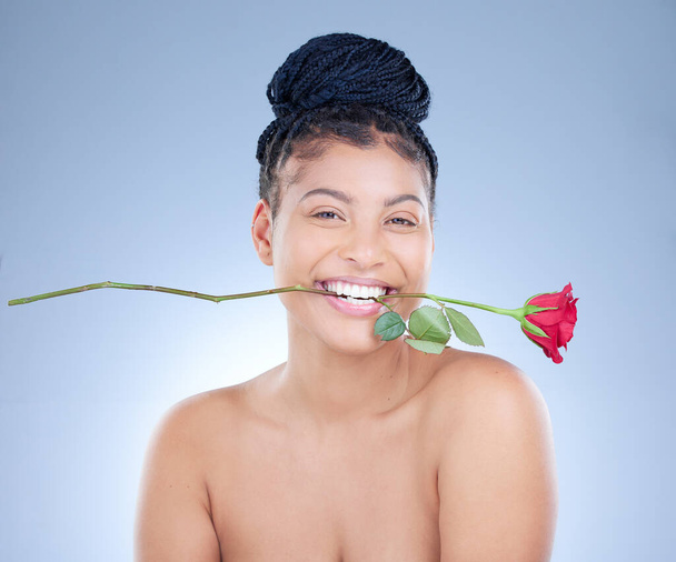 Has naughty ever looked this nice. Studio portrait of an attractive young woman holding a rose between her teeth against a blue background - Photo, Image