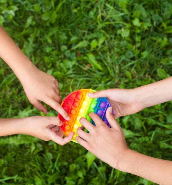 子供の手を丸い虹を保持することはおもちゃをポップ。遊んで。新しいフィジェットトレンディーなおもちゃ。ストレス対策のおもちゃ。シンプルなディンプル. - 写真・画像