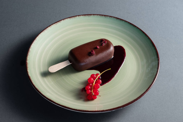 sweet cheesecake popsicle on stick with dark chocolate glaze and fruit filling decorated with red currant on black background - 写真・画像