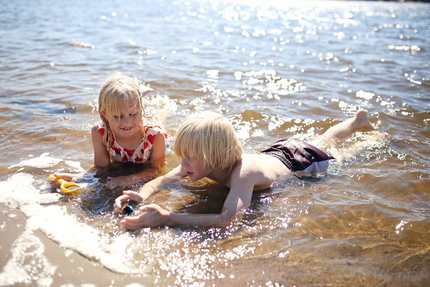 Dos niños están jugando afuera en el agua en la playa en un día de verano.. - Foto, Imagen