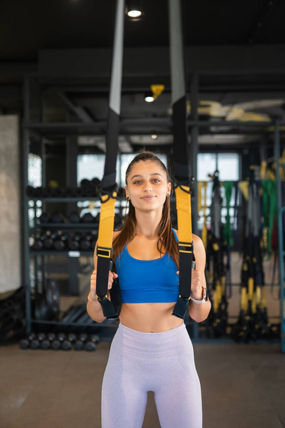 Junge athletische Frau mit perfektem Körper in Sportbekleidung bei Übungen mit Trageschlaufen im Fitnessstudio - Foto, Bild