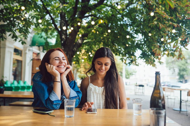 Zwei Freundinnen surfen in Mobiltelefonen, während sie zusammen im Straßencafé der Stadt sitzen. - Foto, Bild