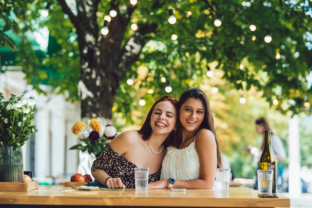 Close-up portrait of two female friends laughing drinking coffee on terrace at summer street cafe on background buildings - Photo, Image