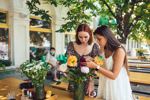 Zwei junge Frauen nehmen Bestellungen entgegen und formen einen schönen festlichen Strauß. Floristik und Herstellung von Sträußen im Straßencafé. Kleinunternehmen. - Foto, Bild