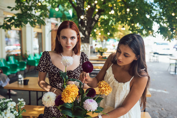 Dos mujeres jóvenes reciben órdenes y conforman un hermoso ramo festivo. Floristería y hacer ramos en el café de la calle. Pequeñas empresas. - Foto, imagen