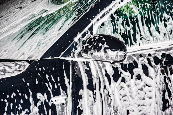 Πλένει το αυτοκίνητο με σαπούνι αφρού. Το αυτοκίνητο είναι καλυμμένο με αφρό.. - Φωτογραφία, εικόνα