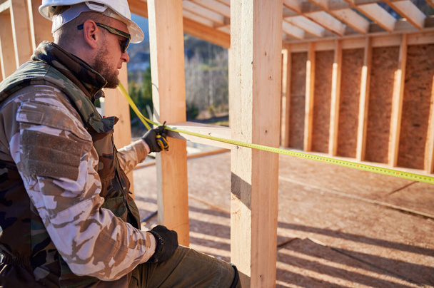 Mies työntekijä rakentaa puinen runko talo. Puuseppä mittanauhalla mittaamiseen puulaudat. Puusepäntyöt. - Valokuva, kuva