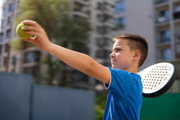 Спортивний молодий хлопчик з ракеткою грає на велюрі у відкритому дворі на відкритому повітрі
 - Фото, зображення
