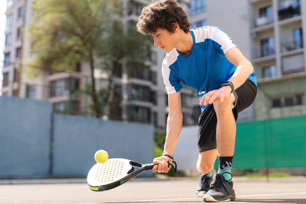 Sportive young boy with racquet playing padel in the open court outdoors - Photo, image