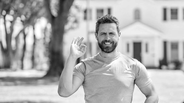 щасливий зрілий чоловік ріелтор, що стоїть на відкритому повітрі в будинку, показує добре жест, купуючи будинок
. - Фото, зображення