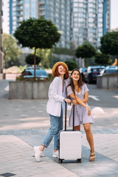Two young women with a suitcase pose for the camera on the street - Foto, Imagen