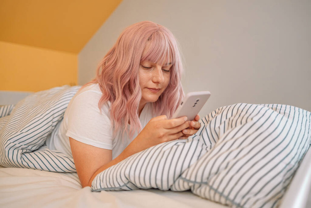 Mujer relajada usando un teléfono inteligente en la mañana en la cama en casa - Foto, Imagen