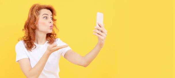 女の子の携帯電話の黄色の背景に手を接吻ジェスチャーを作る、モバイルデバイス。女性隔離された顔の肖像画、モックアップ付きバナーコピースペース - 写真・画像
