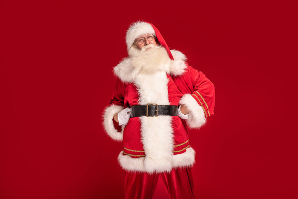 Happy bearded Santa Claus smiling to the camera, posing on red studio background. Merry Christmas and Happy New Year! A lot of copy space. Xmas sale, discount concept - Valokuva, kuva