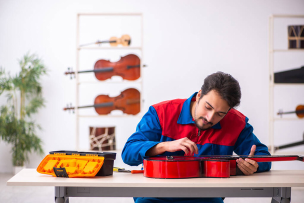 İş yerinde müzik aletlerini tamir eden genç bir tamirci. - Fotoğraf, Görsel