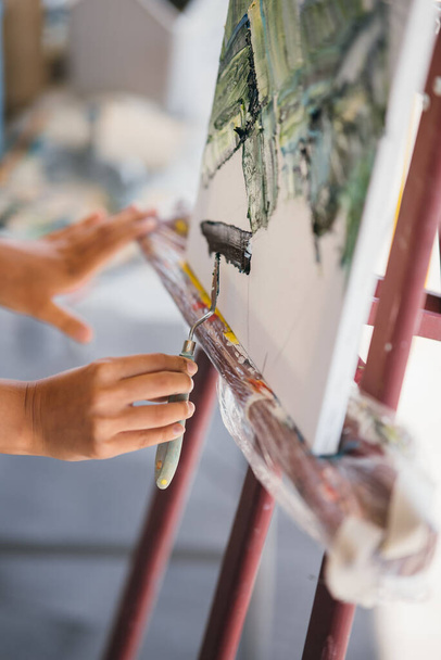 Primo piano di una mano di donne che applica vernice su una tela con una spatola - Foto, immagini