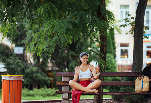 Happy girl using a smartphone in a city park sitting on a bench - Fotó, kép