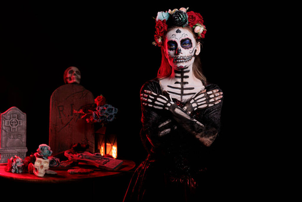 Beautiful woman wearing santa muerte costume on day of the dead holiday tradition, posing in studio. Model with horror catrina skull body art looking like holy goddess of death. - Photo, Image