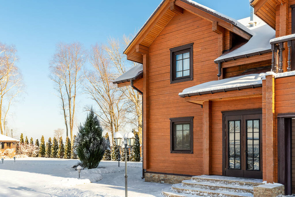 Scenery facade front view of modern wooden luxury timber eco house villa with garage door snowcapped by white fresh snow at cold sunny winter day. Real estate building construction project exterior. - Fotó, kép