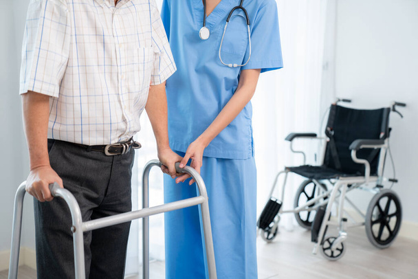 Physiotherapist assists contented senior man on folding walker. Recuperation for elderly, seniors care, nursing home. - Zdjęcie, obraz