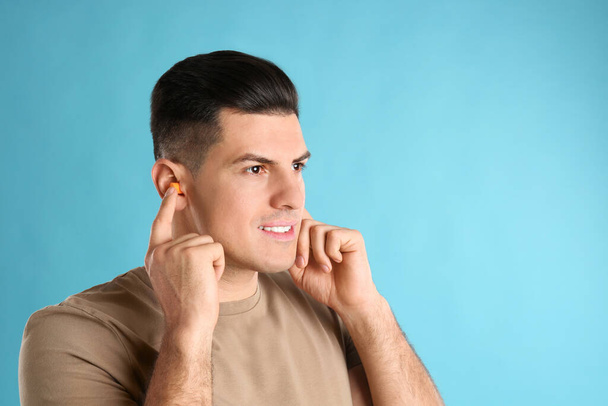 Man inserting foam ear plugs on light blue background. Space for text - Foto, imagen