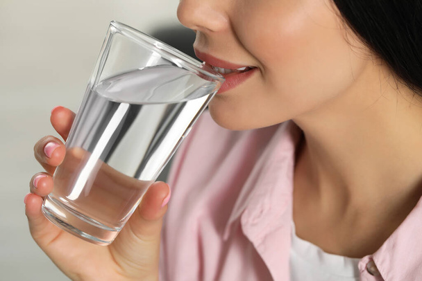 Young woman drinking water indoors, closeup. Refreshing drink - Fotó, kép