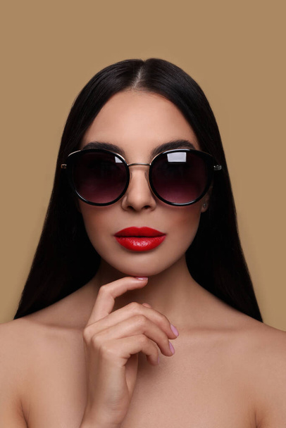 Attractive woman in fashionable sunglasses touching her face against beige background - Valokuva, kuva
