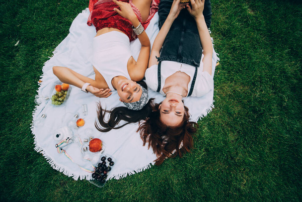 Дві жінки мають пікнік разом, лежачи на підлозі на газоні
 - Фото, зображення