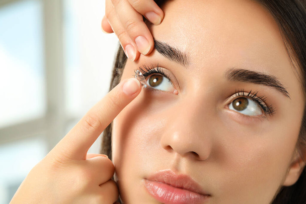 Woman putting contact lens in her eye indoors, closeup view - Zdjęcie, obraz