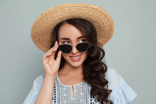 Beautiful young woman with straw hat and stylish sunglasses on light grey background - Photo, image