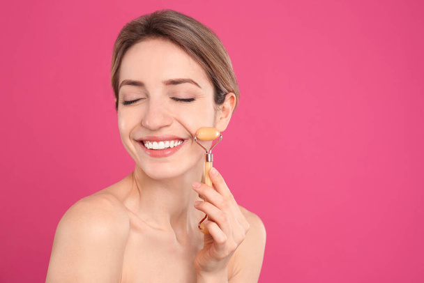Young woman using natural jade face roller on pink background, space for text - Fotoğraf, Görsel