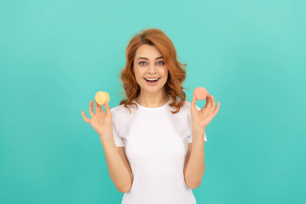 glimlachende vrouw houden zoete macaron frans koekje op blauwe achtergrond. - Foto, afbeelding