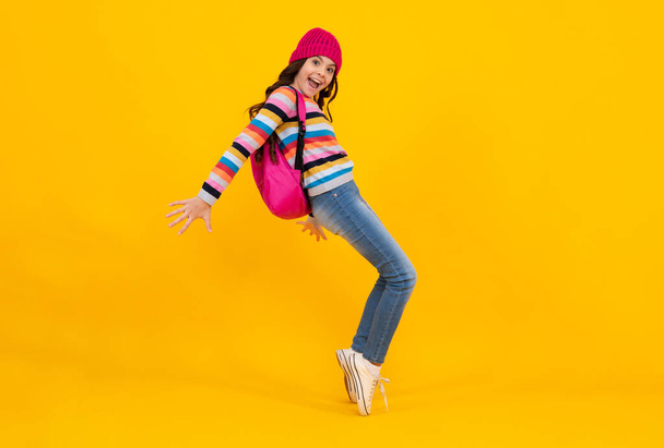 Winter school. Teenager school girl with backpack in autumn clothes on yellow isolated studio background. Happy teenager, positive and smiling emotions of teen girl - Фото, зображення
