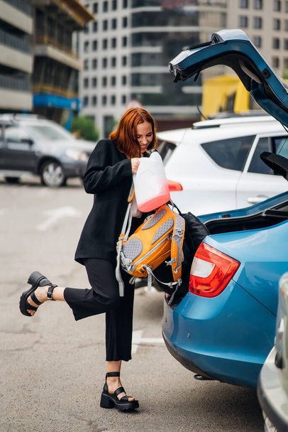 Una giovane donna sta mettendo i bagagli nel bagagliaio dell'auto. - Foto, immagini