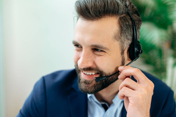 Közelkép fotó egy pozitív kaukázusi férfi headset, call center munkavállaló, szakértő, vállalati képviselő, támogató szolgáltató, tart online konzultáció ügyfél, néz oldalra, mosolygós - Fotó, kép
