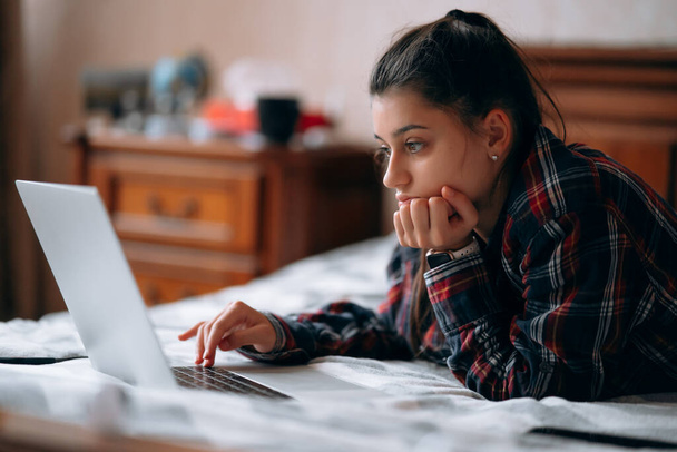 Focus selettivo di lavoro giovane donna mentre con il computer portatile sdraiato sul letto - Foto, immagini