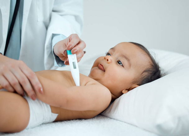 Comprobando si hay síntomas de fiebre. un pediatra que toma la temperatura de un bebé con un termómetro en una clínica - Foto, imagen