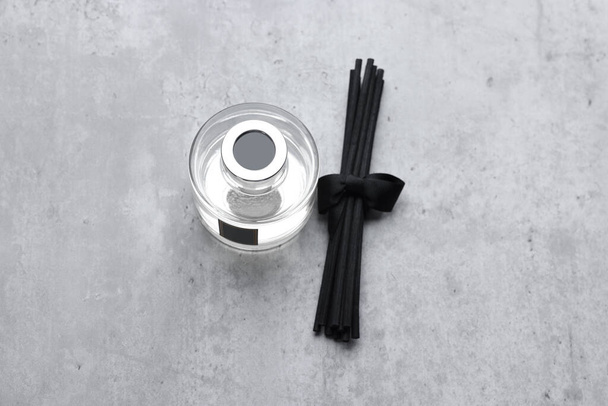 Reed sticks near glass bottle with aromatic liquid on gray marble table, flat lay - Photo, image