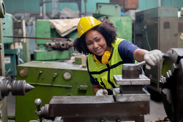 Concept of technician heavy industry, Woman African American engineer wear hardhat working at machine in factory. Female technician control metalwork lathe industrial.  - Photo, Image
