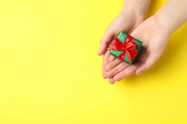 Woman holding beautifully wrapped Christmas gift box on yellow background, top view. Space for text - Valokuva, kuva