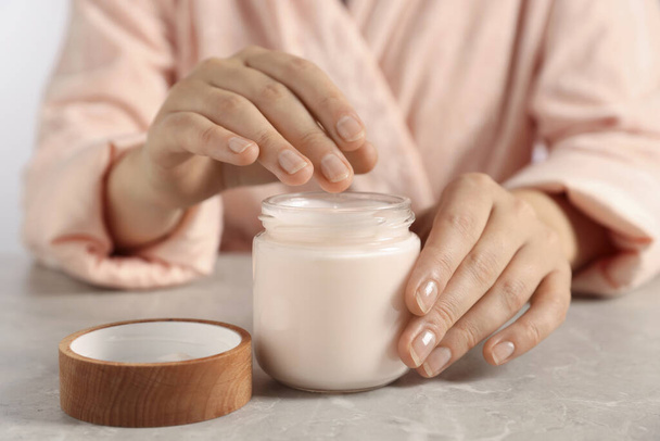 Woman applying hand cream at grey table, closeup - Zdjęcie, obraz