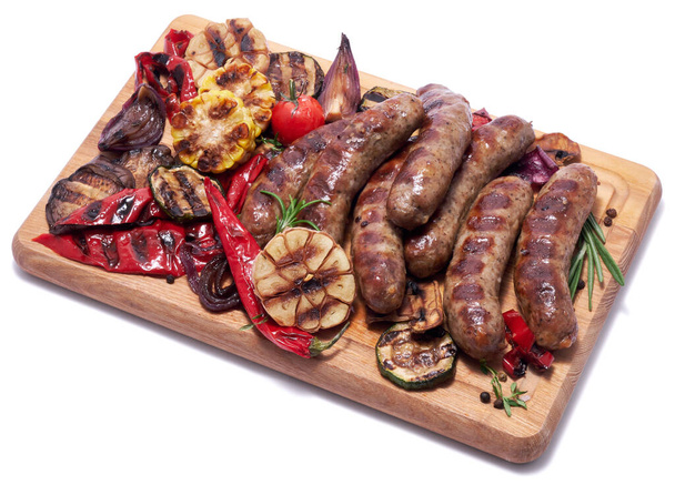 Grilled sausages and vegetables on wooden cutting board isolated on white background. - Photo, image