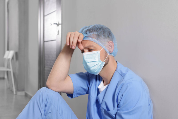 Exhausted doctor near grey wall in hospital corridor - Фото, изображение