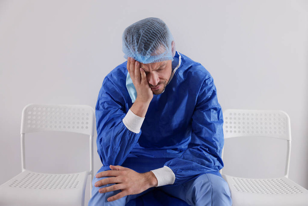 Exhausted doctor sitting on chair near grey wall - Photo, Image