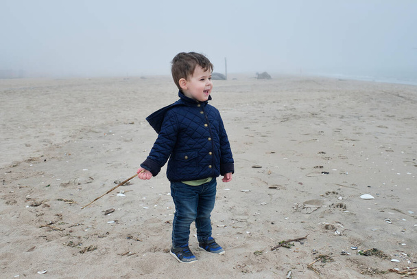 Młody chłopiec bawiący się kijem na plaży - Zdjęcie, obraz